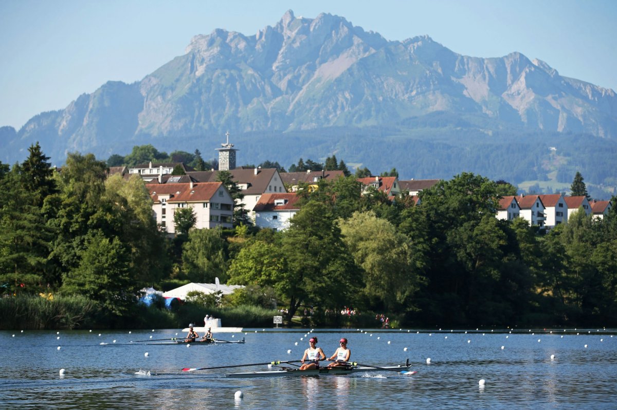 white buildings red roofs green trees people rowing on the water mountains in the background