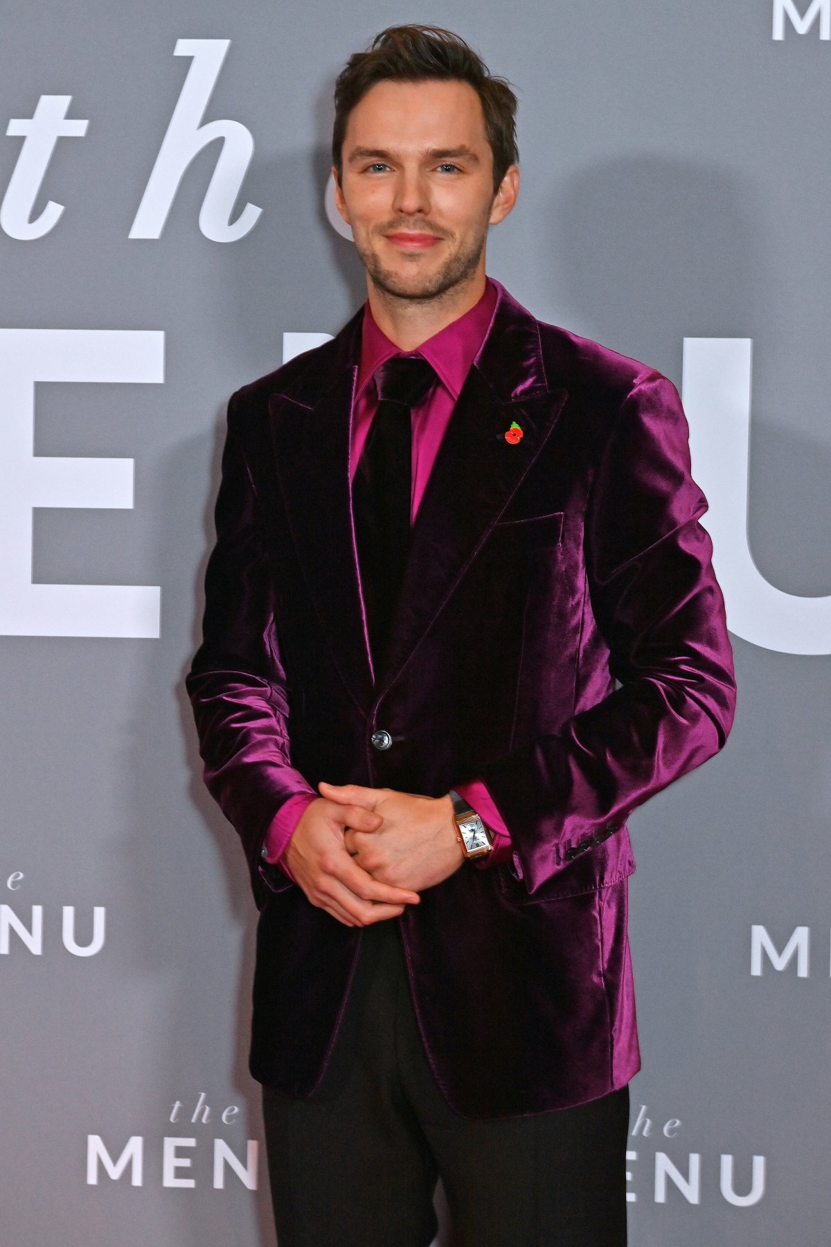 Nicholas Hoult in a burgandy velvet suit on a grey background.