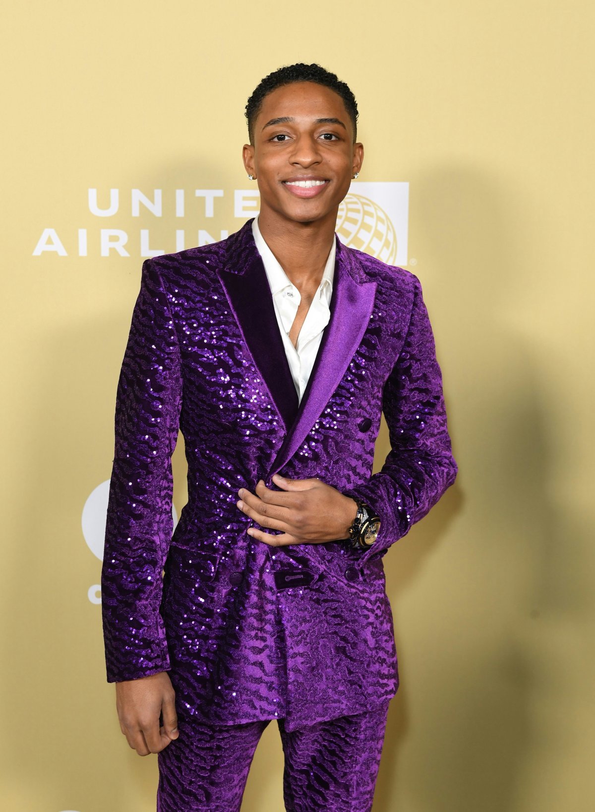 Myles Frost in a purple suit on a yellow background.