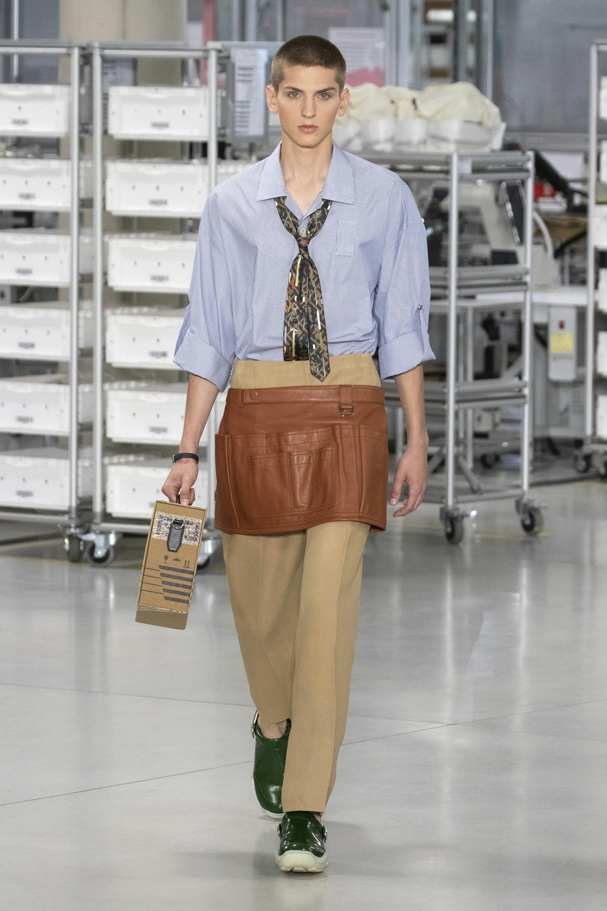 A model in a button down shirt, trousers, and brown utility skirt.