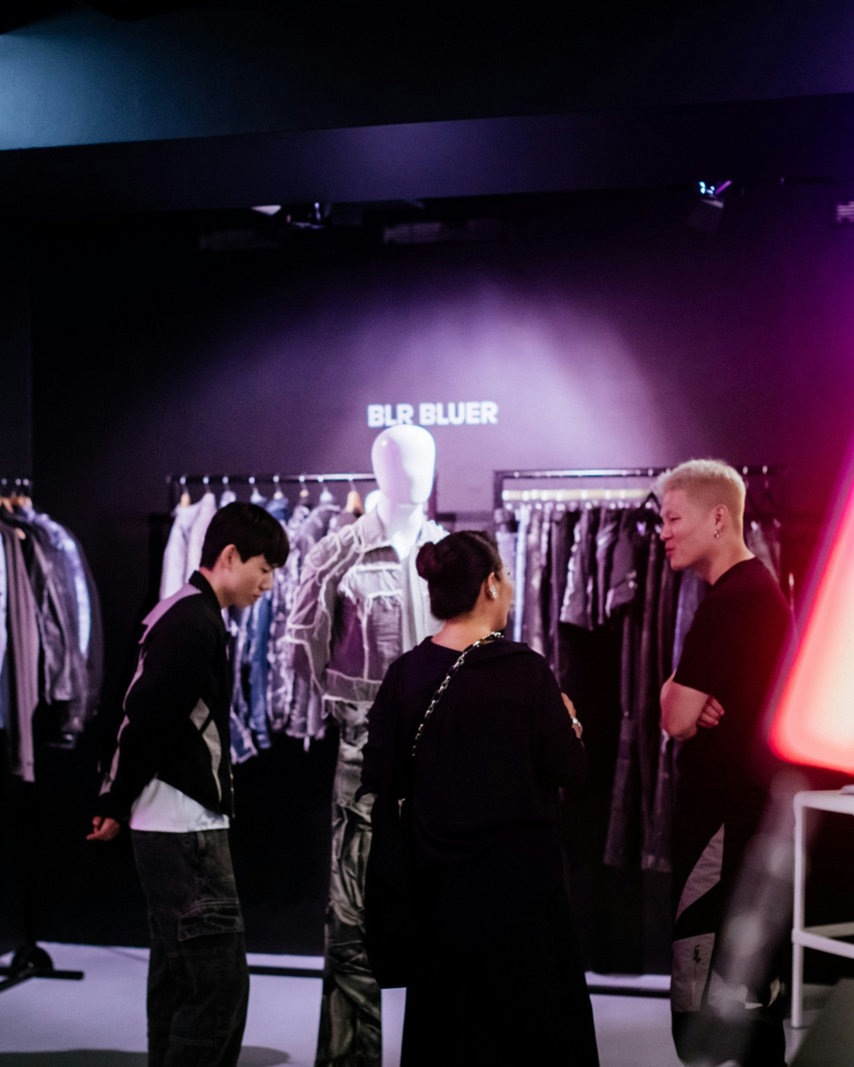 Three people standing in front of mannequin and racks of clothes. Photo via Instagram/ @seoulfashionweek_official