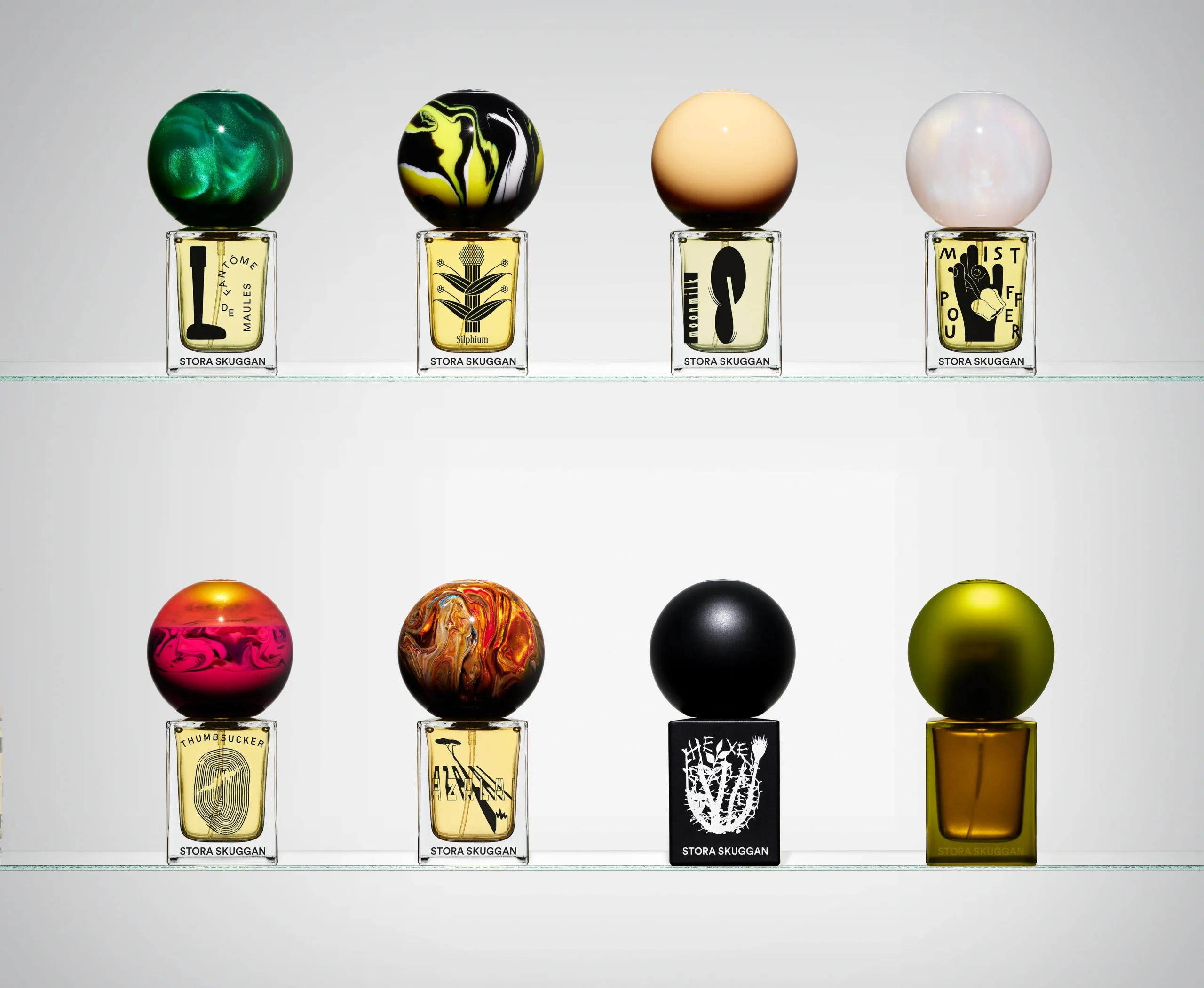 A collection of Stora Skuggan perfume bottles featuring unique spherical caps displayed on two glass shelves.